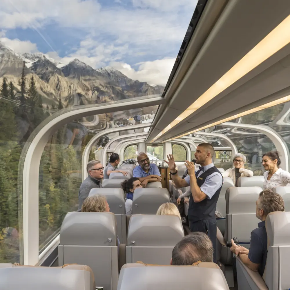 Vue intérieure d'un wagon du train Rocky Mountaineer de la classe de service GoldLeaf avec son dôme vitré et l'hôte à bord qui donne des explications aux passagers