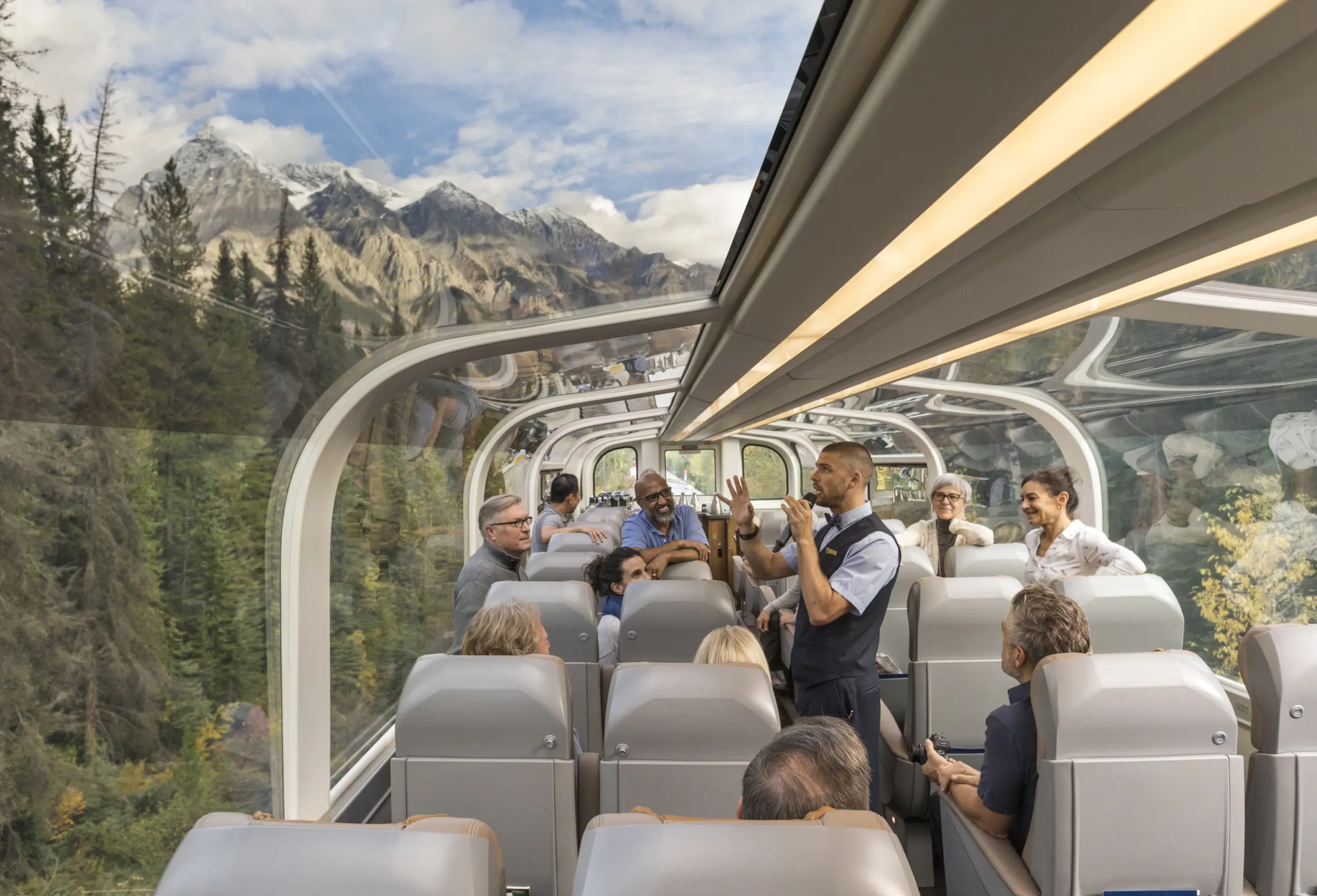 Vue intérieure d'un wagon du train Rocky Mountaineer de la classe de service GoldLeaf avec son dôme vitré et l'hôte à bord qui donne des explications aux passagers