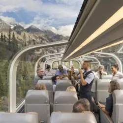 Vue intérieure d'un wagon du train Rocky Mountaineer de la classe de service GoldLeaf avec son dôme vitré et l'hôte à bord qui donne des explications aux passagers