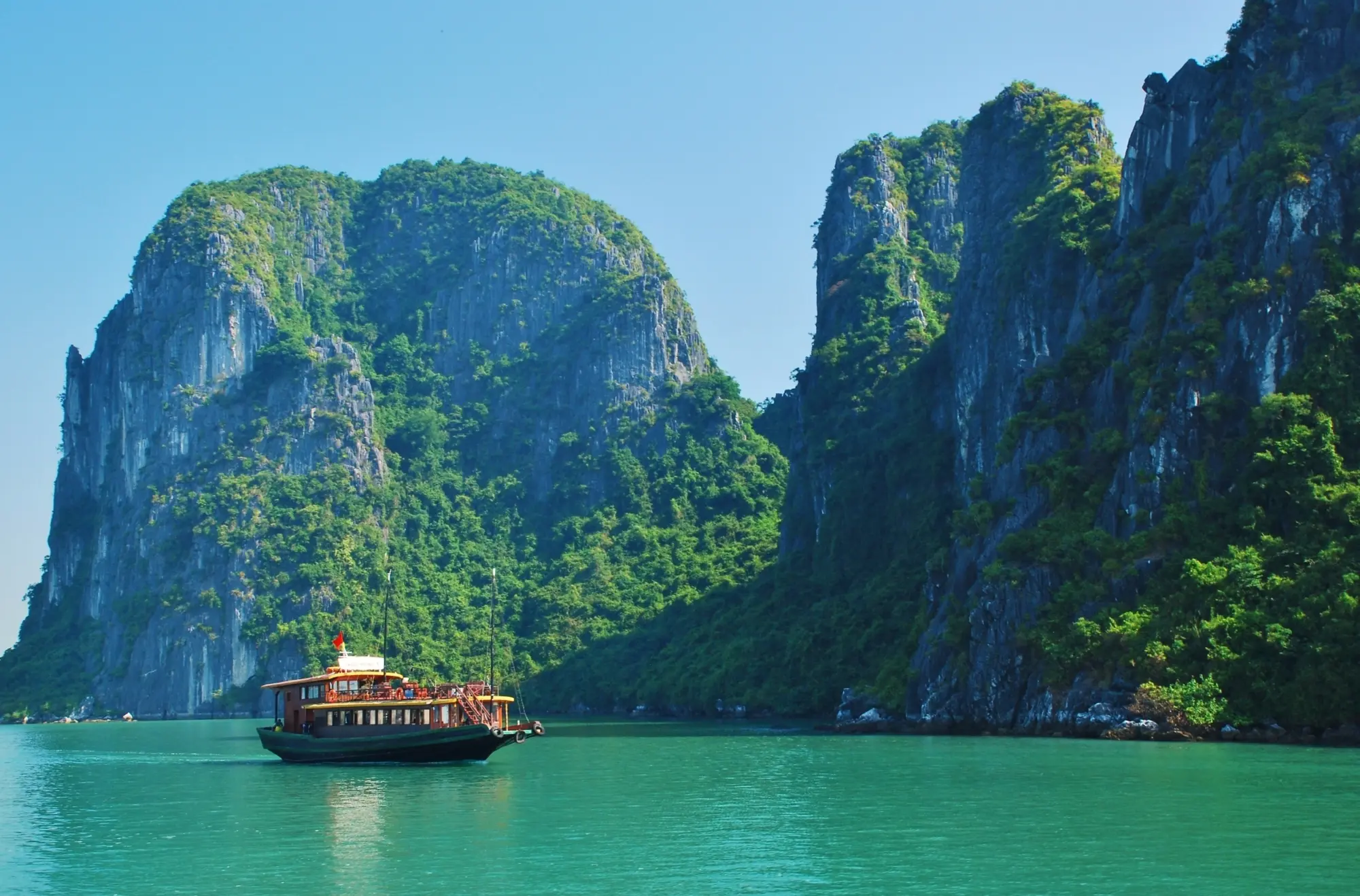 Un bateau sur une eau turquoise entouré de montagnes au Vietnam