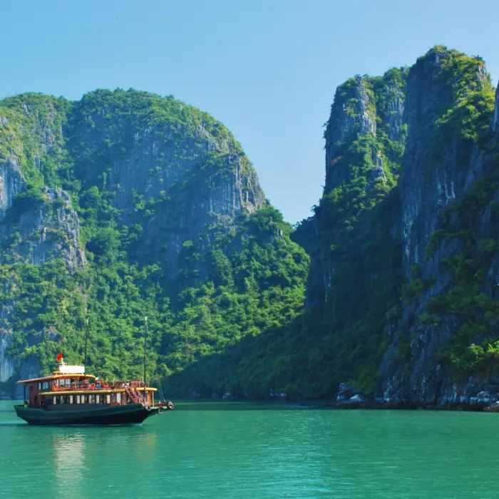 Un bateau sur une eau turquoise entouré de montagnes au Vietnam