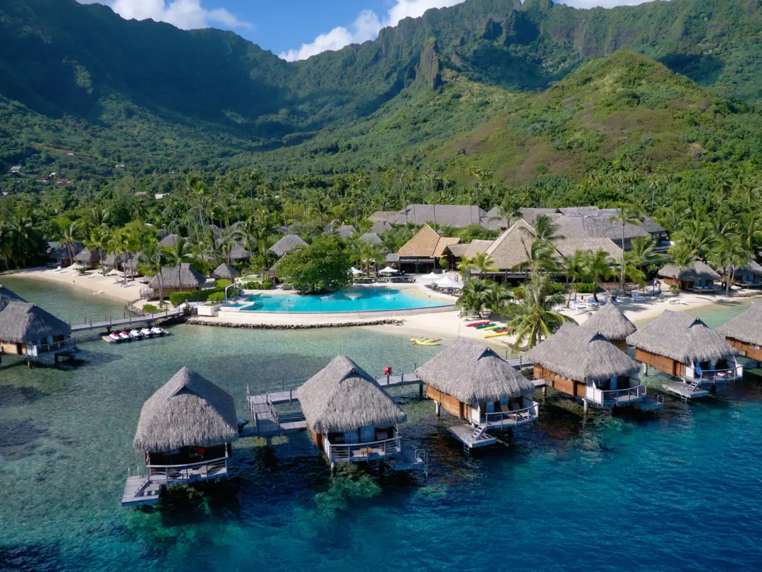 Vue sur les bungalows et la piscine du  Manava Beach Resort & Spa Hotel Moorea en Polynésie française, avec en arrière-plan de grandes montagnes