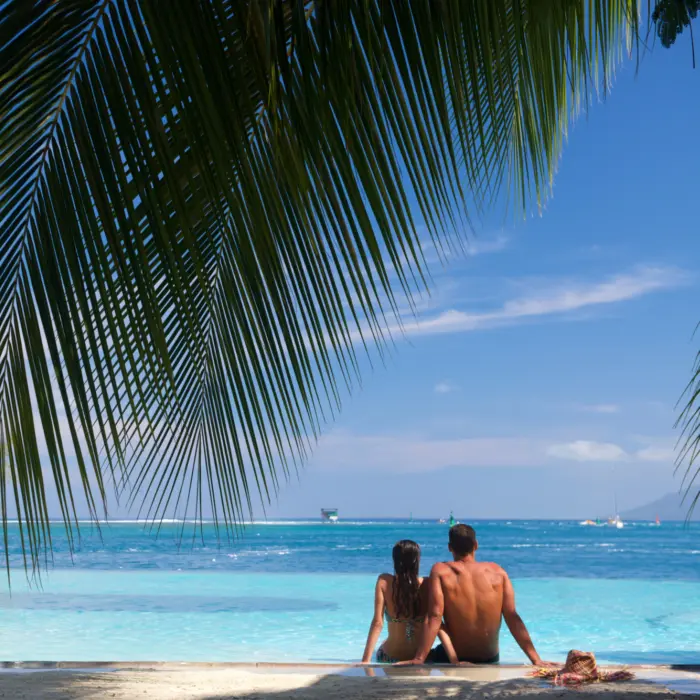 Un couple sur la plage de sable de l'hôtel Te Moana Tahiti Resort en Polynésie française, admirant l'océan turquoise