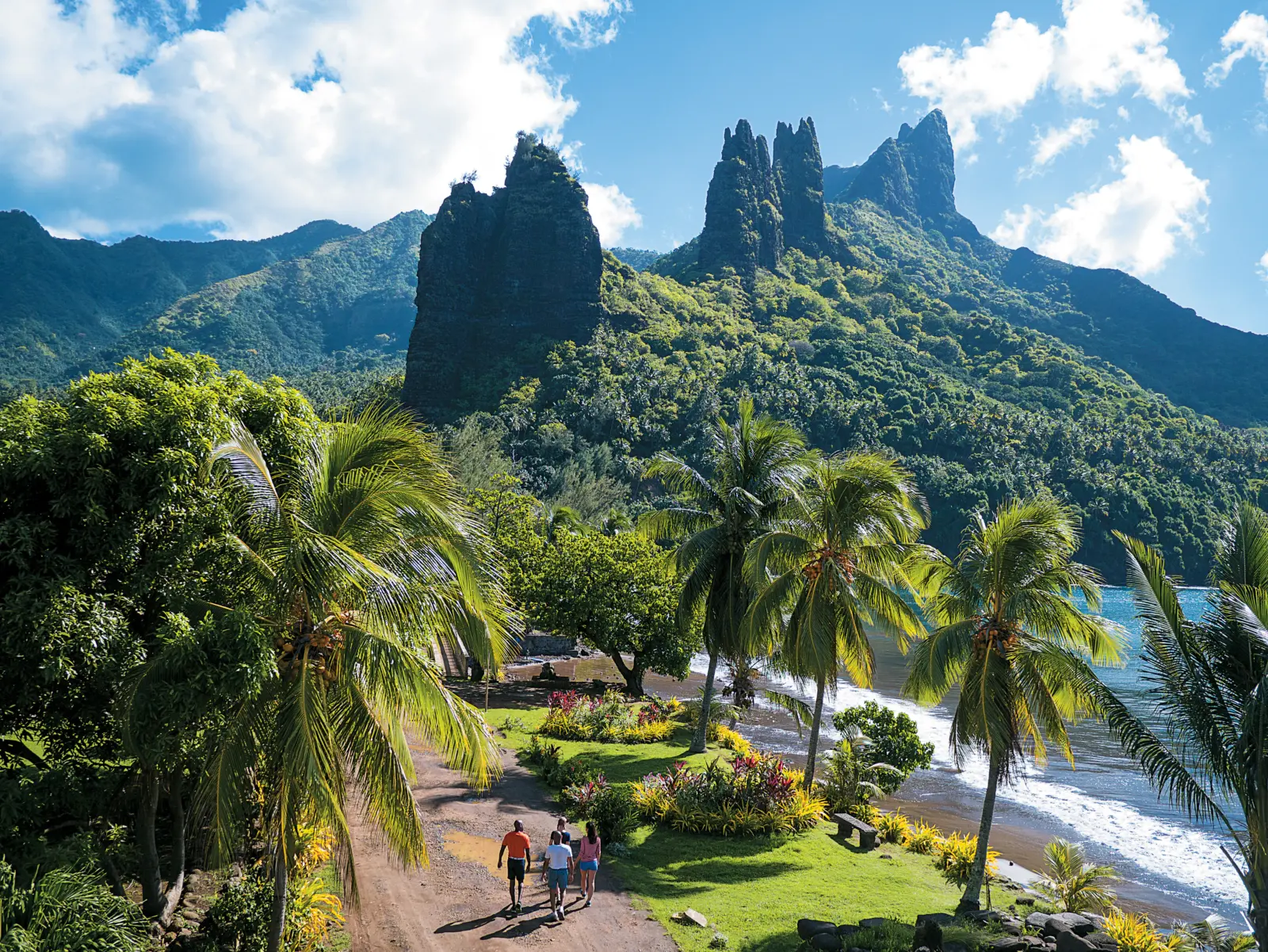 Chemin côtier bordé de palmiers, menant à une vue imprenable sur les pics volcaniques de Nuku Hiva, aux Marquises