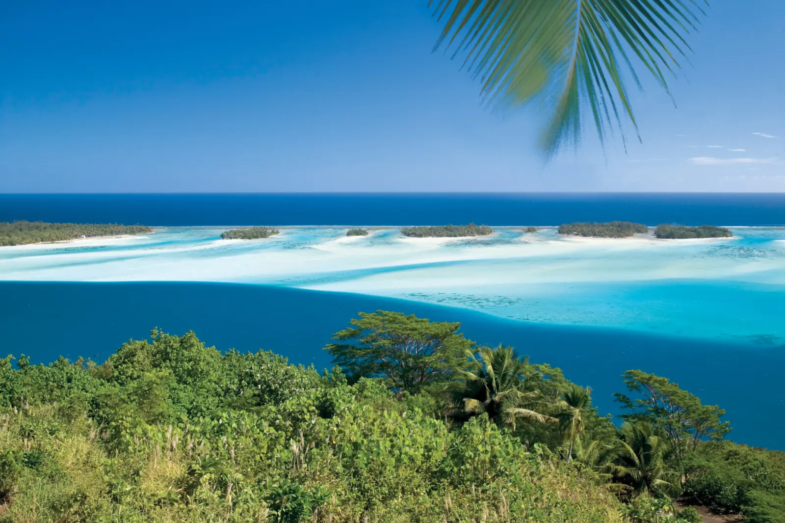 Vue aérienne d'un lagon turquoise aux eaux cristallines, entouré d'îlots de sable blanc à Bora Bora en Polynésie française